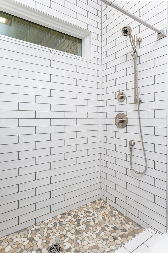 Close-up of walk-in shower with pebble tile flooring and white subway tile