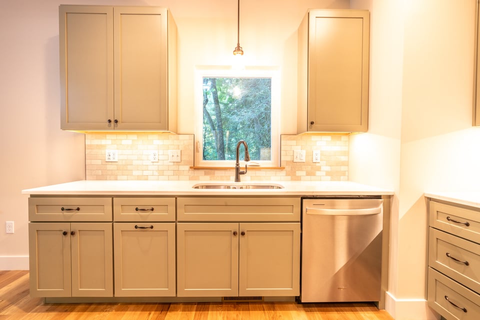 Elegant kitchen design with green cabinets and stainless dishwasher by Kaizen Home