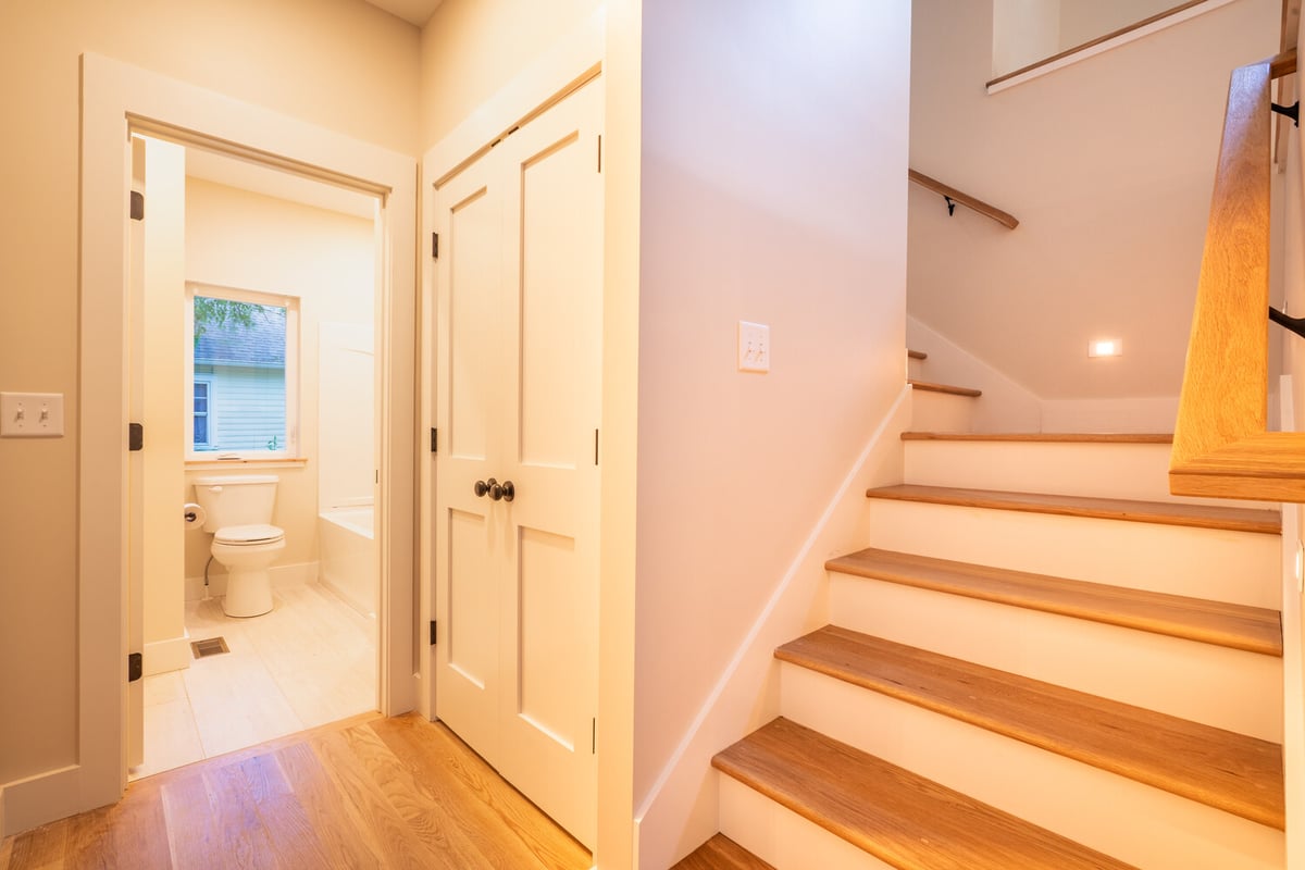Modern hallway with bright lighting and hardwood stairs in a Kaizen Homes