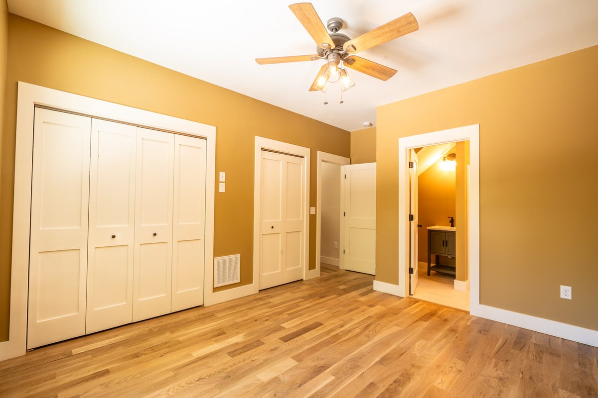 Warm-toned bedroom with ceiling fan and bathroom doorway by Kaizen Homes
