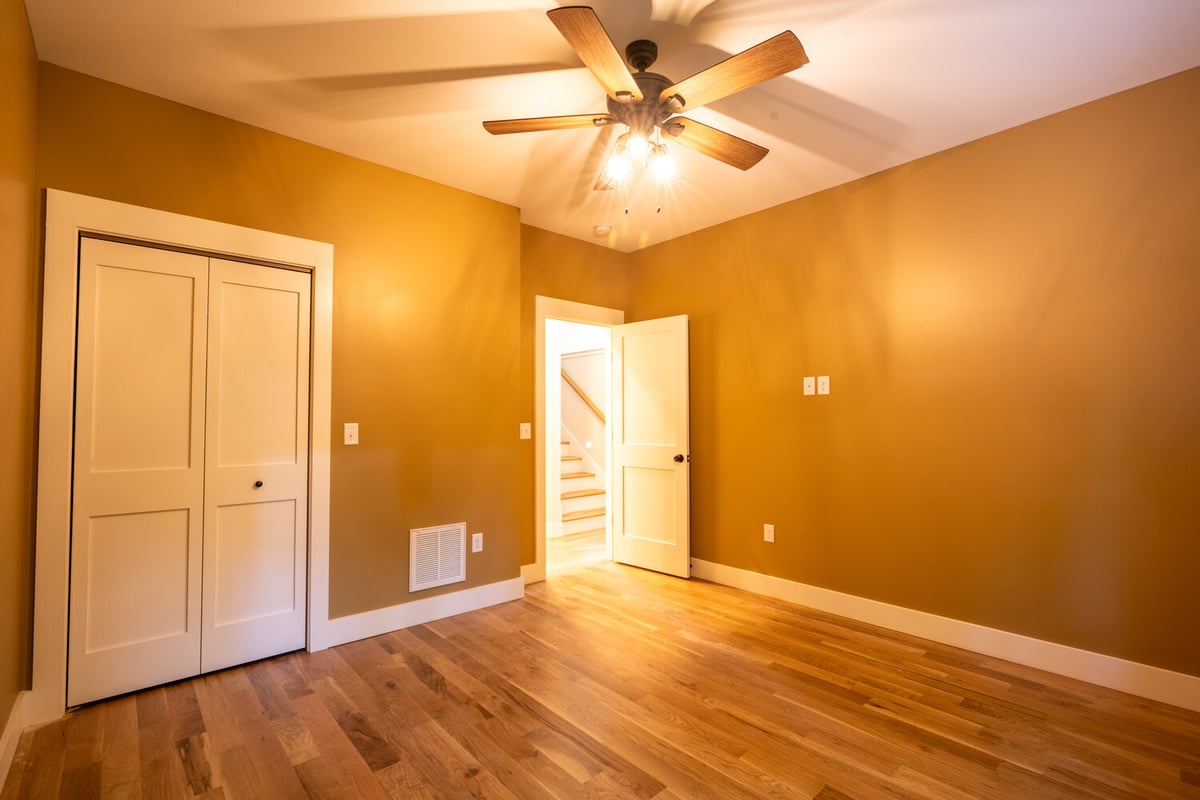 Warm-toned bedroom with wood floors and ceiling fan in Kaizen Homes build