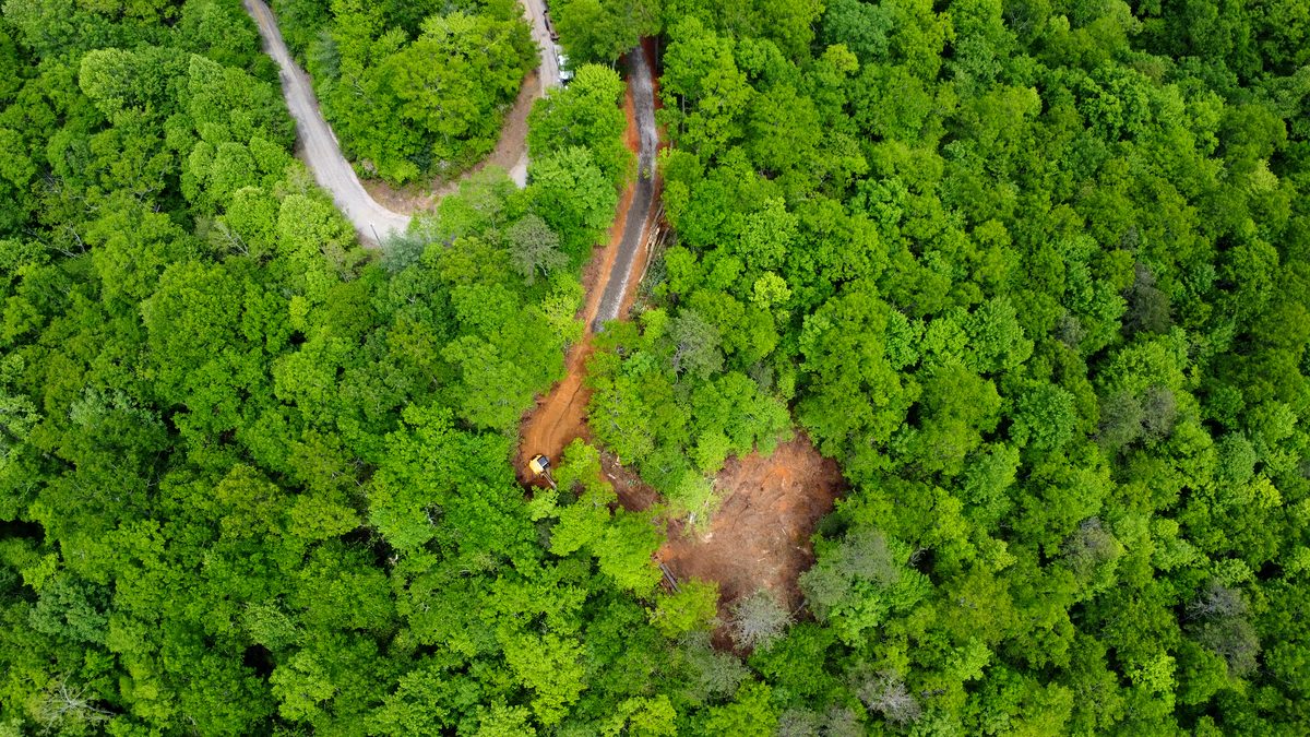 Aerial view of WNC mountain lot with winding driveway cut through dense forest during site preparation